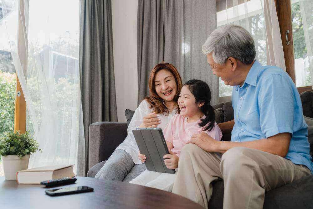 grandmother and grandfather laughing with their granddaughter at a tablet screen