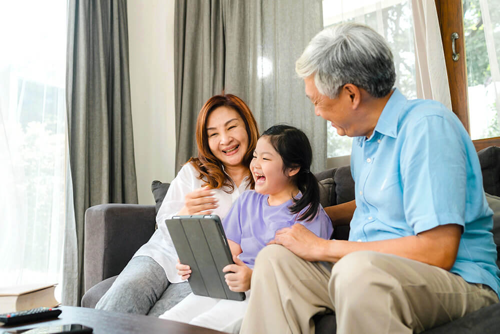 Asian grandparents enjoy watching shows on a tablet with grand daughter