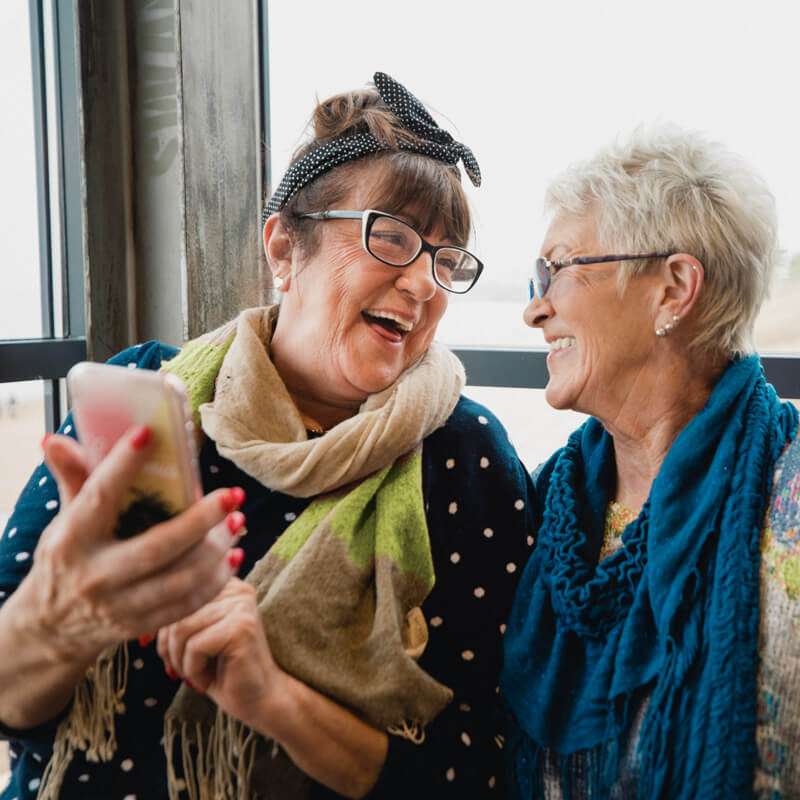 Two women laugh while looking at a smart phone