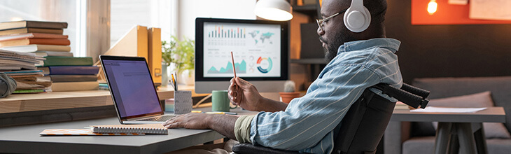 Data professional seated in a wheelchair works from home with a multi-device setup and headphones