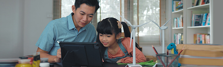 Dad and daughter on a tablet explore online together in a craft and STEM hobby room where she is building a wind turbine model