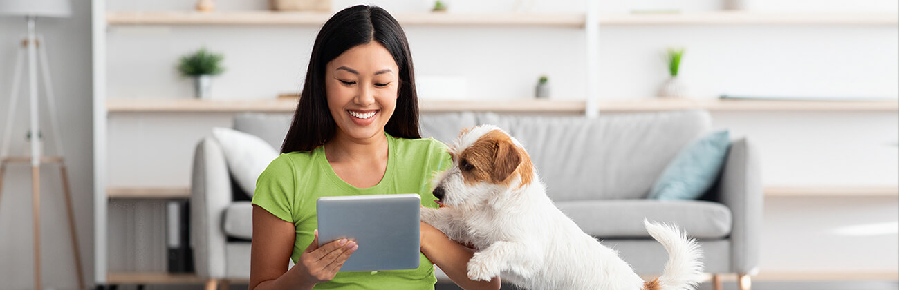 Smiling dark-haired woman with small fluffy dog quickly browses her tablet before walk time