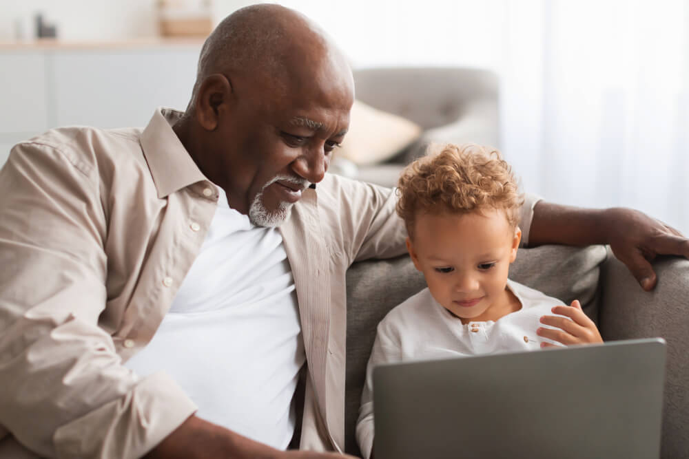 Grandfather watches as his grandson learns about Black History Month on laptop